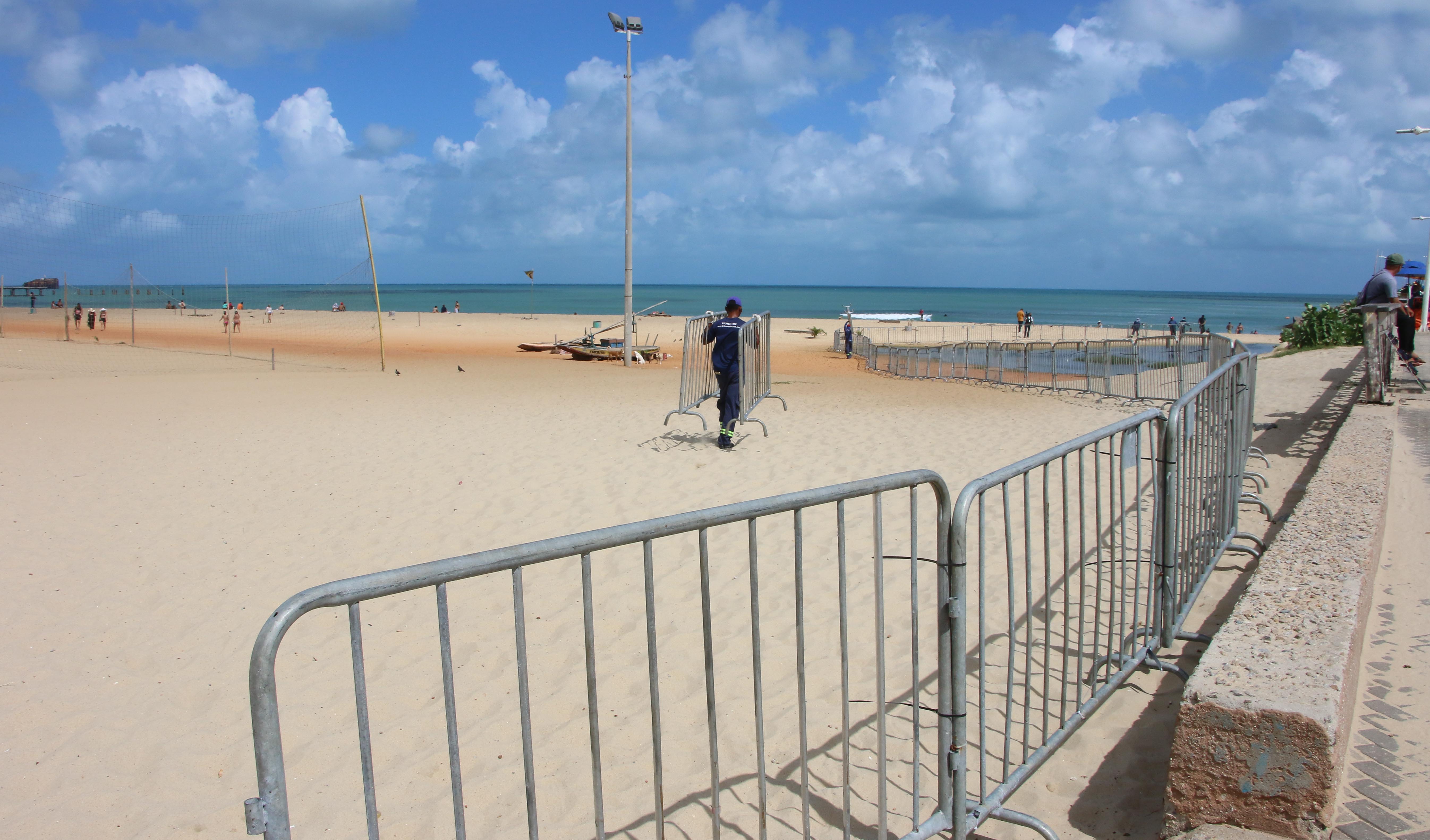 faixa de areia com mar ao fundo, gradis montados ao lado direito e homem de costas carregando dois gradis no meio